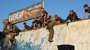entrants at tough mudder help each other climb a wall